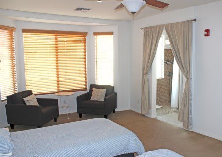 A cozy bedroom featuring two chairs by a large window, with neutral decor and an adjoining bathroom.