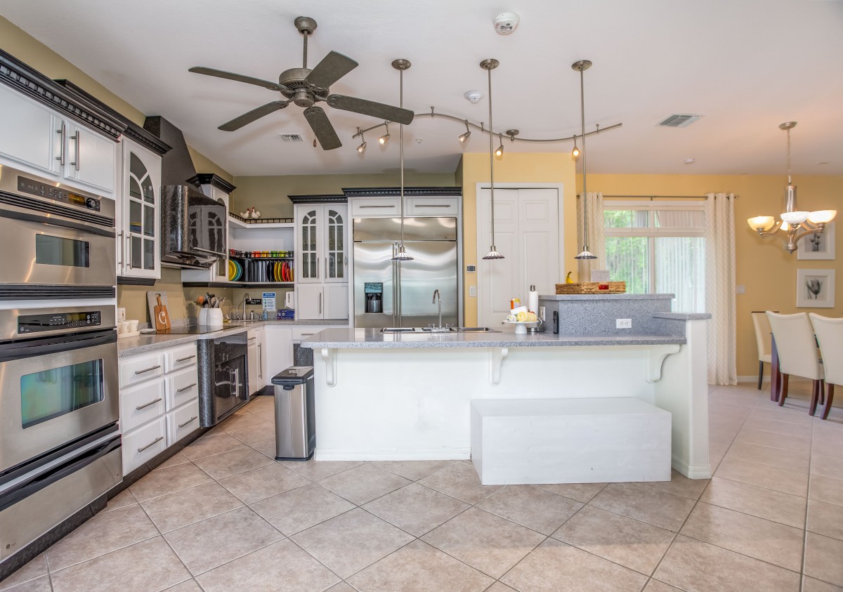 A modern kitchen with white cabinetry and a spacious island, featuring pendant lighting and tile flooring.