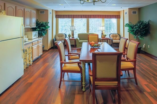 A spacious dining room with a large table, elegant chairs, and warm hardwood floors, featuring a kitchen area and large windows that allow natural light to fill the space.