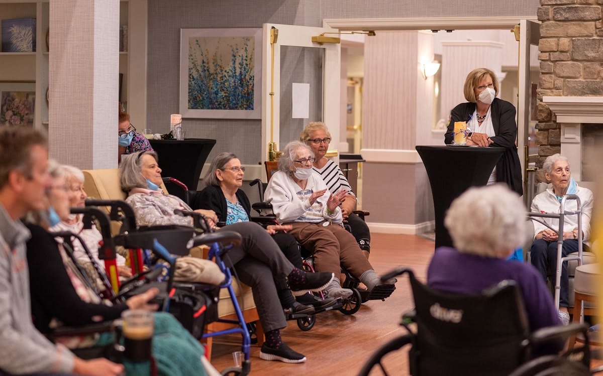 A group of elderly people gathered in a nursing home, seated in wheelchairs and chairs, attending a social event.