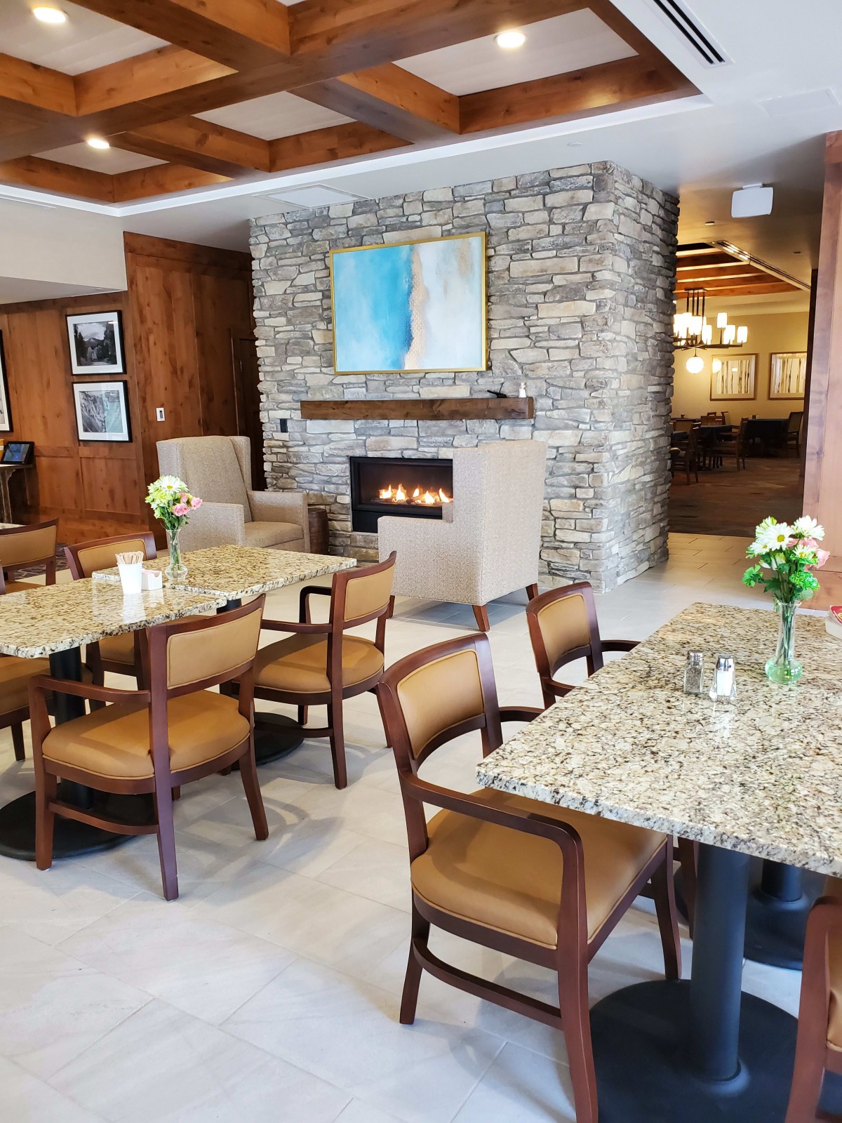 A cozy dining area with granite tables, wooden chairs, a stone fireplace, and elegant decor.