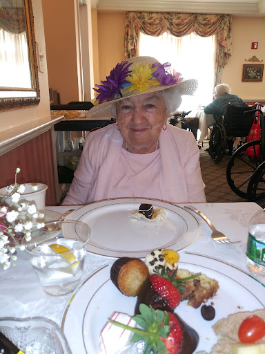 A joyful elderly woman wearing a colorful hat, enjoying a festive meal with dessert.