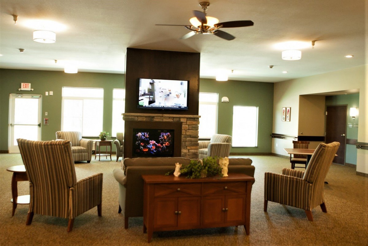 A cozy living area featuring a television above a fireplace, surrounded by comfortable seating and warm lighting.