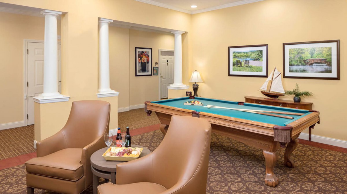 A cozy game room featuring a pool table and leather seating, accented by wall art and a warm color scheme.