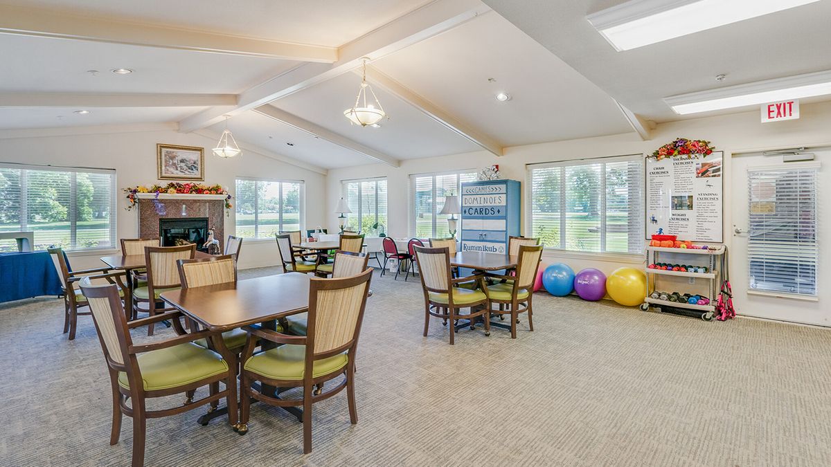 A bright and spacious community lounge area with tables, chairs, and colorful gym balls.