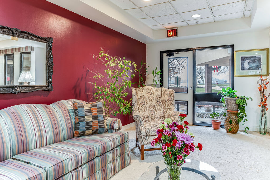 A cozy lobby with a striped sofa, patterned armchair, and vibrant plants and flowers.