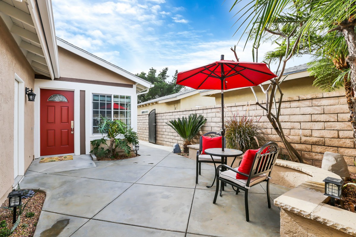 A cozy patio area with a red umbrella and seating set against the backdrop of a house exterior.