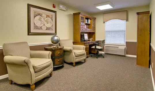 A cozy office space with comfortable armchairs, a wooden bookshelf, and a decorative globe.
