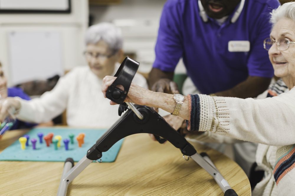 A caregiver assists an elderly person with physical therapy exercises using specialized equipment.
