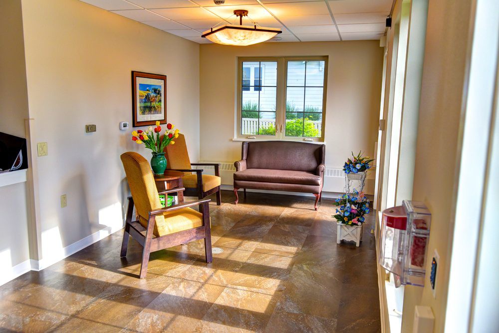 A cozy waiting room with chairs, a table, and sunlight streaming through the window.