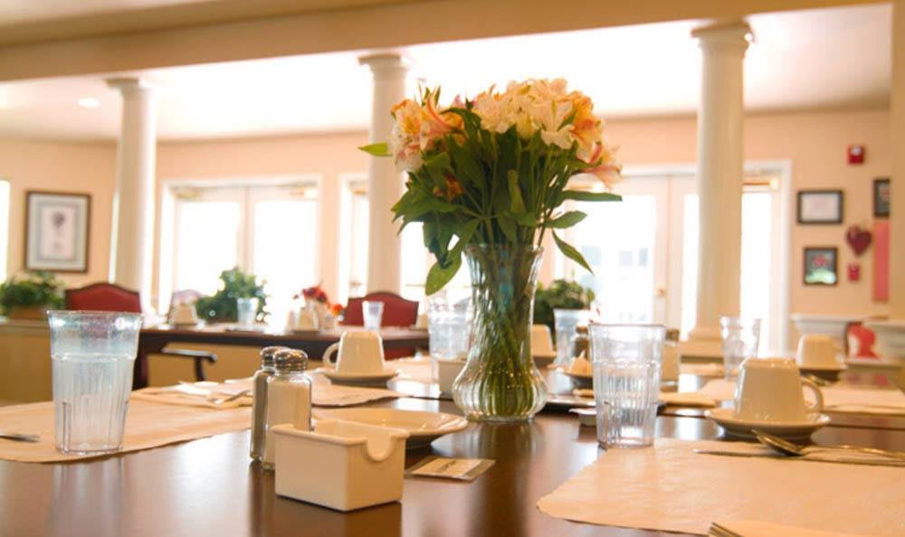 A beautifully set dining table with a vase of flowers in a well-lit restaurant.