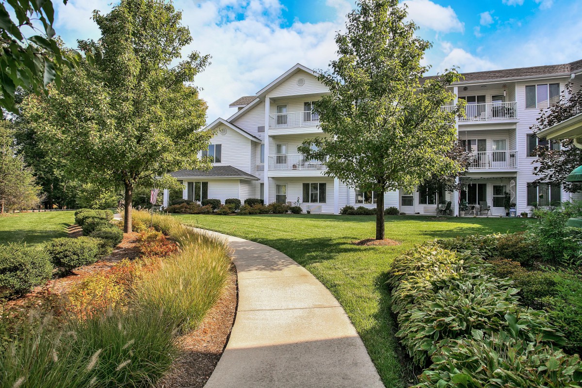 A scenic view of a residential building with a winding pathway surrounded by lush greenery and trees.