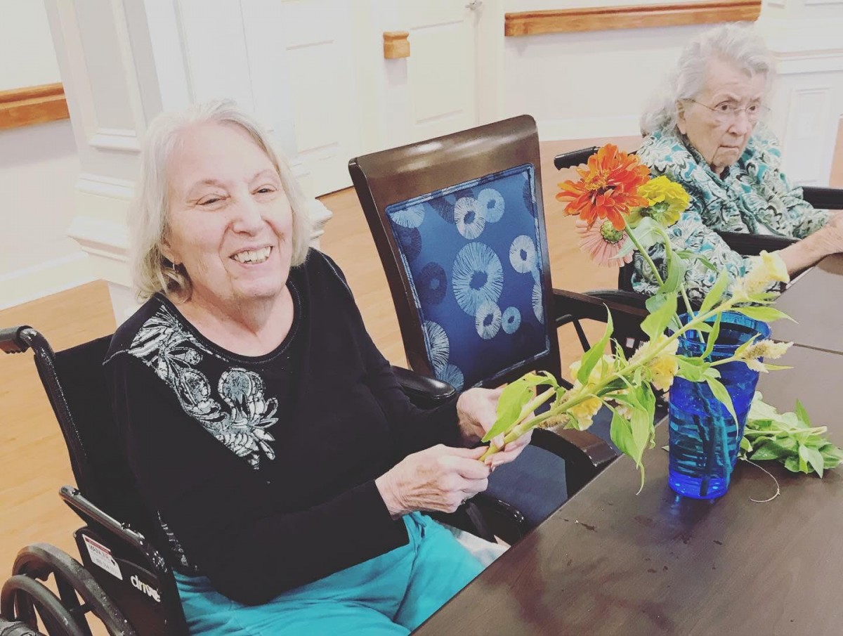 Two elderly women enjoying a moment with flowers indoors.