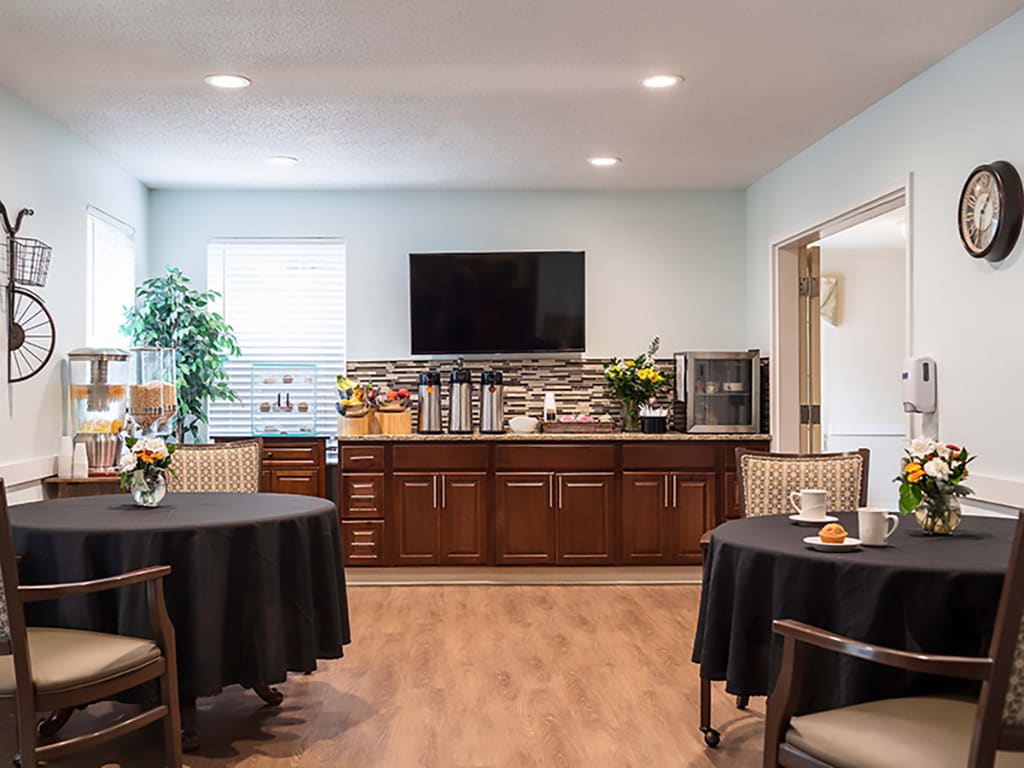 A modern dining area with round tables, chairs, and a television mounted above wooden cabinets.