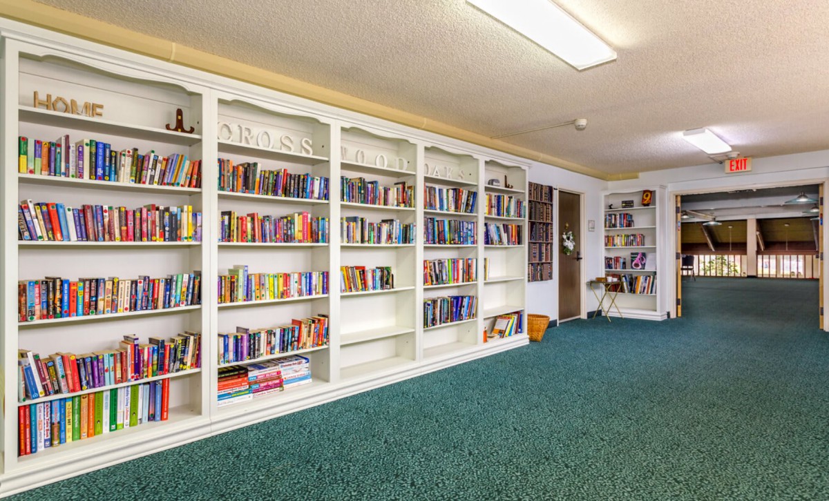 A cozy library room with white bookshelves filled with a variety of books and green carpeted flooring.