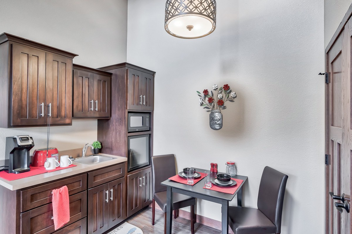 A cozy kitchen nook with a small dining table set for two, surrounded by modern wood-finished cabinets and a stylish hanging light fixture.
