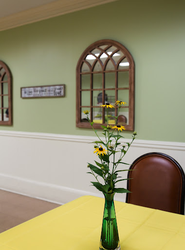 A cozy dining area featuring a cheerful yellow tablecloth and a vase of sunflowers, complemented by green walls and decorative mirrors.