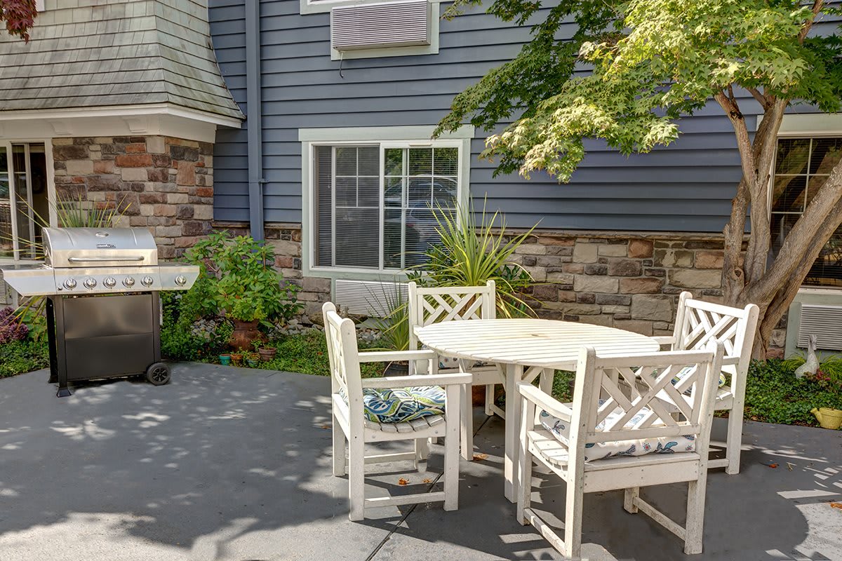 A cozy patio area with a round table and white chairs surrounded by plants and a stone facade.