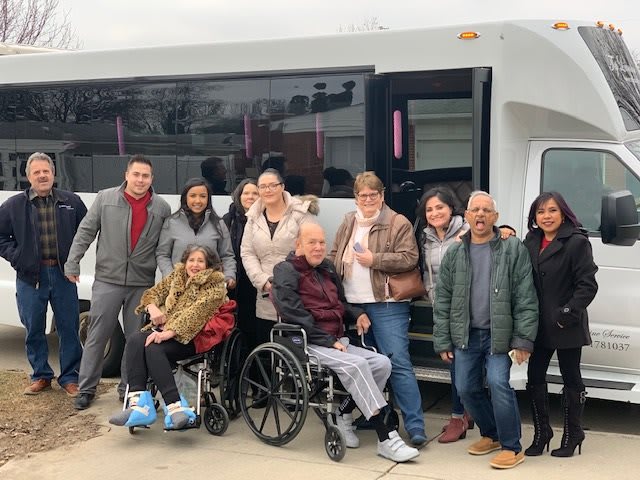 A diverse group of people, including two individuals in wheelchairs, stand happily in front of a bus.