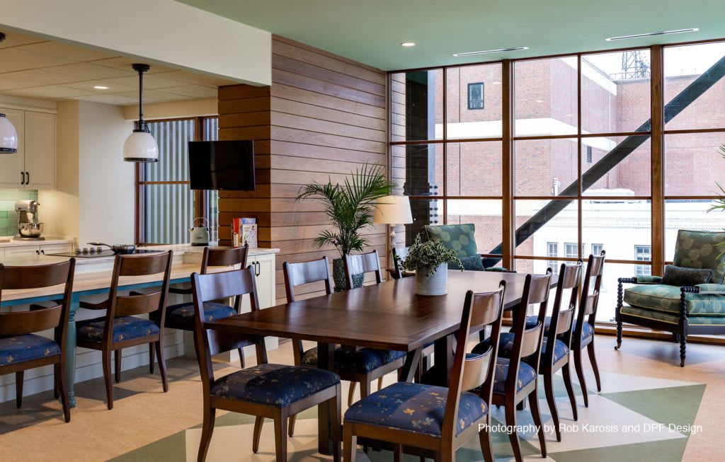 A modern dining area with wooden tables and chairs, featuring large windows that allow natural light to flood the space.