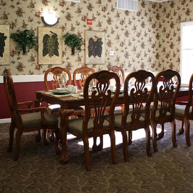 A traditional dining room with a large wooden table and chairs, featuring patterned wallpaper and decorative art pieces on the walls.
