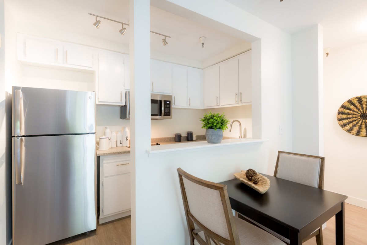 A modern apartment kitchen with white cabinets and a dining area featuring stainless steel appliances.