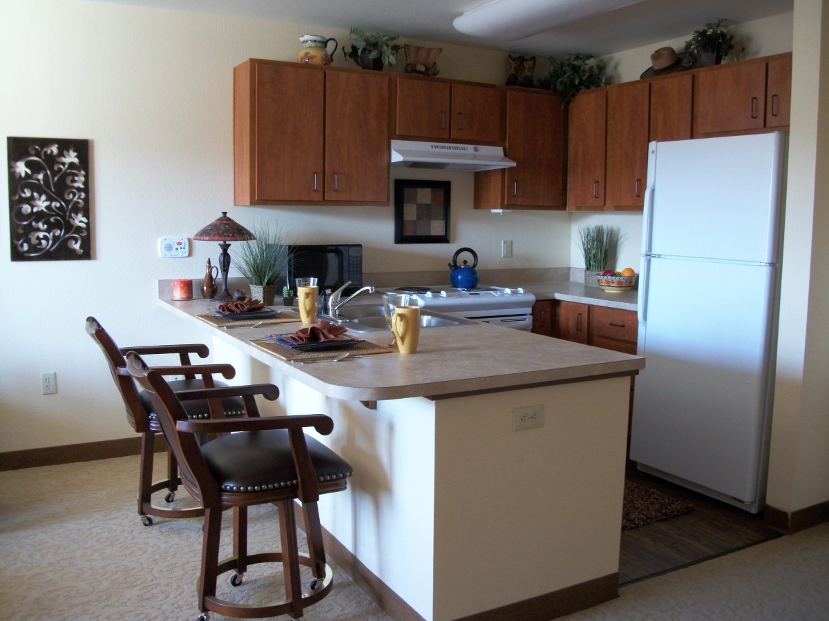A modern kitchen with wooden cabinets, a large white refrigerator, and a countertop with bar stools.