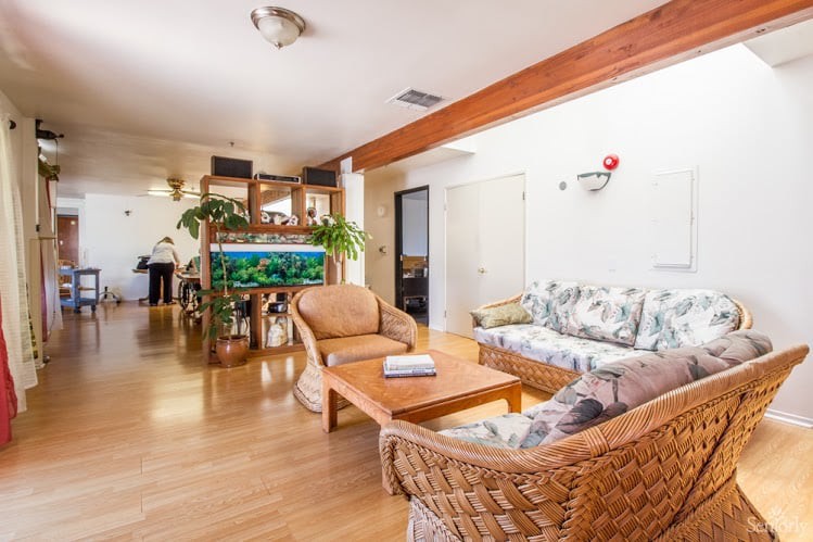 A cozy living room with a sofa set, coffee table, and an aquarium, accentuated by plants and wood flooring.