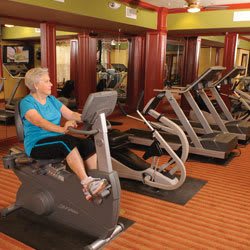 A person exercising on a stationary bike in a gym filled with fitness equipment.
