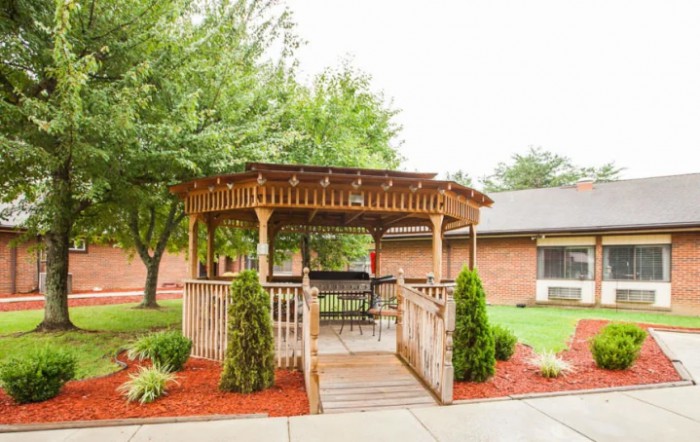 A wooden gazebo surrounded by landscaped gardens and a concrete pathway.