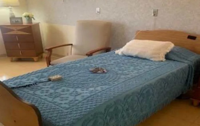A neatly made bed with a blue blanket in a room featuring chairs and other furniture.