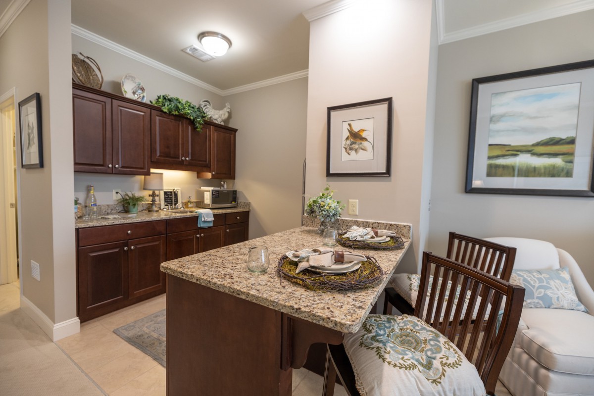 A cozy kitchen area with wooden cabinets and a granite countertop island featuring decorative plants and seating.