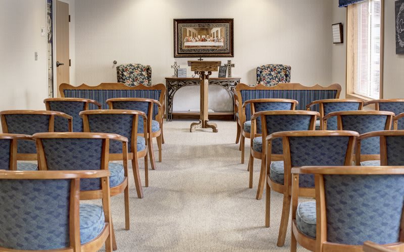 An empty chapel interior with rows of wooden chairs and a central pulpit.