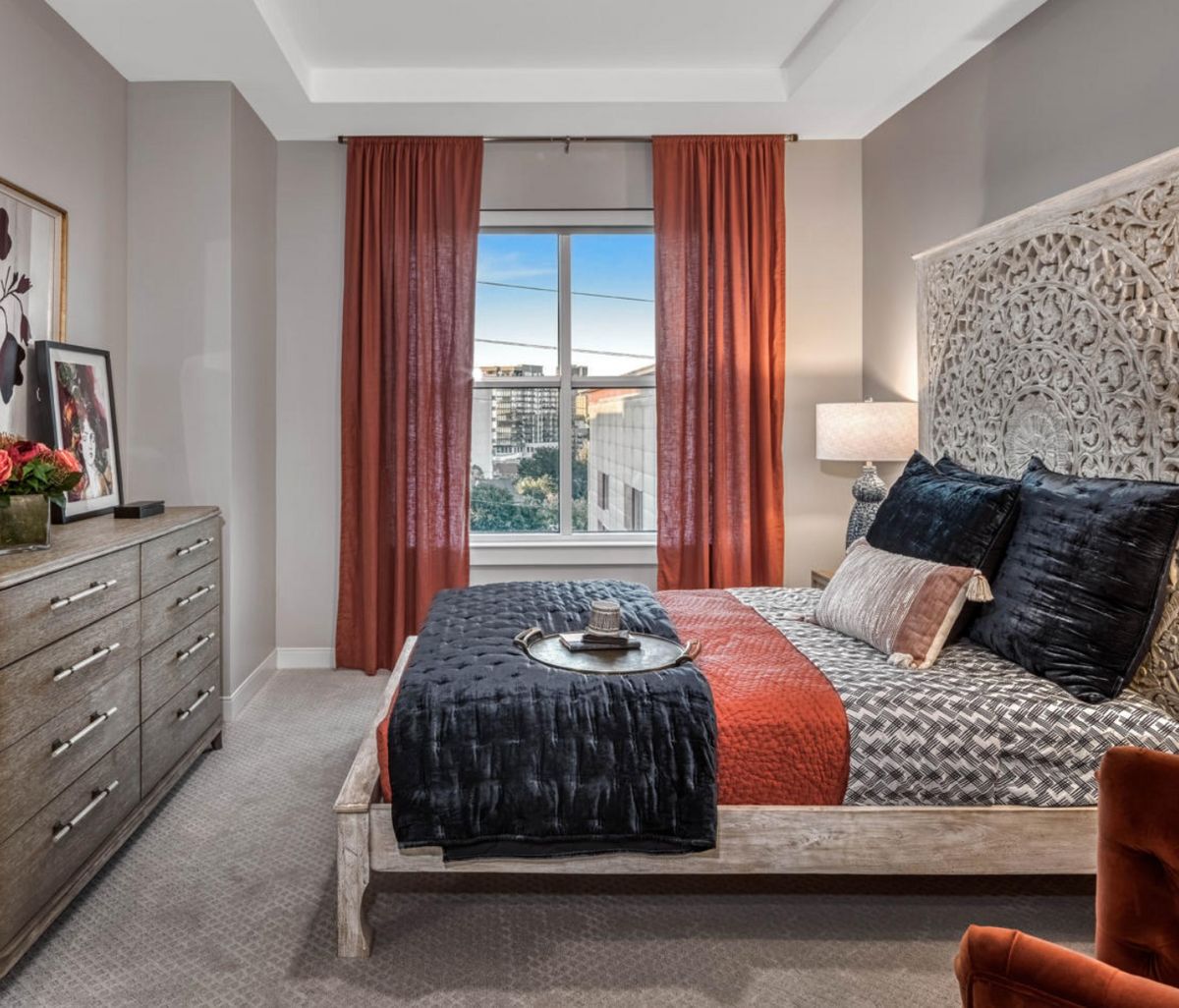 A stylishly designed bedroom featuring vibrant orange accents and a window with a city view.