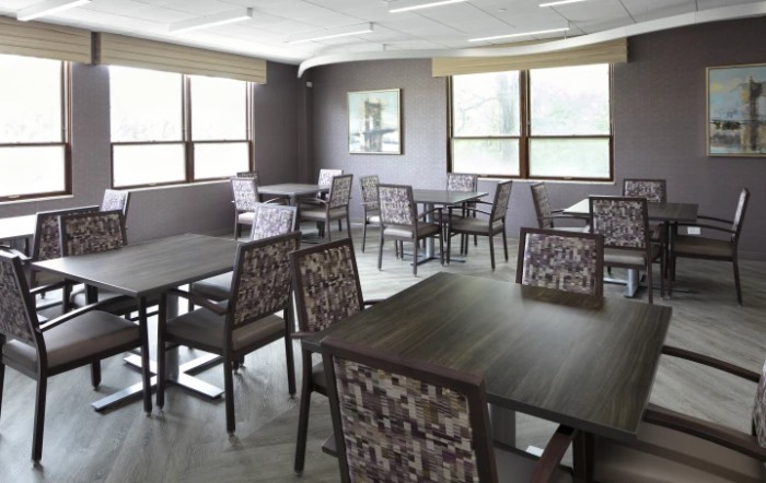 An empty dining area with multiple tables and chairs, well-lit by natural light from the windows.