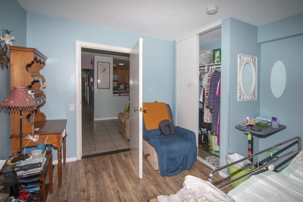 A bedroom with an open closet filled with clothes, featuring a chair and a light blue wall.