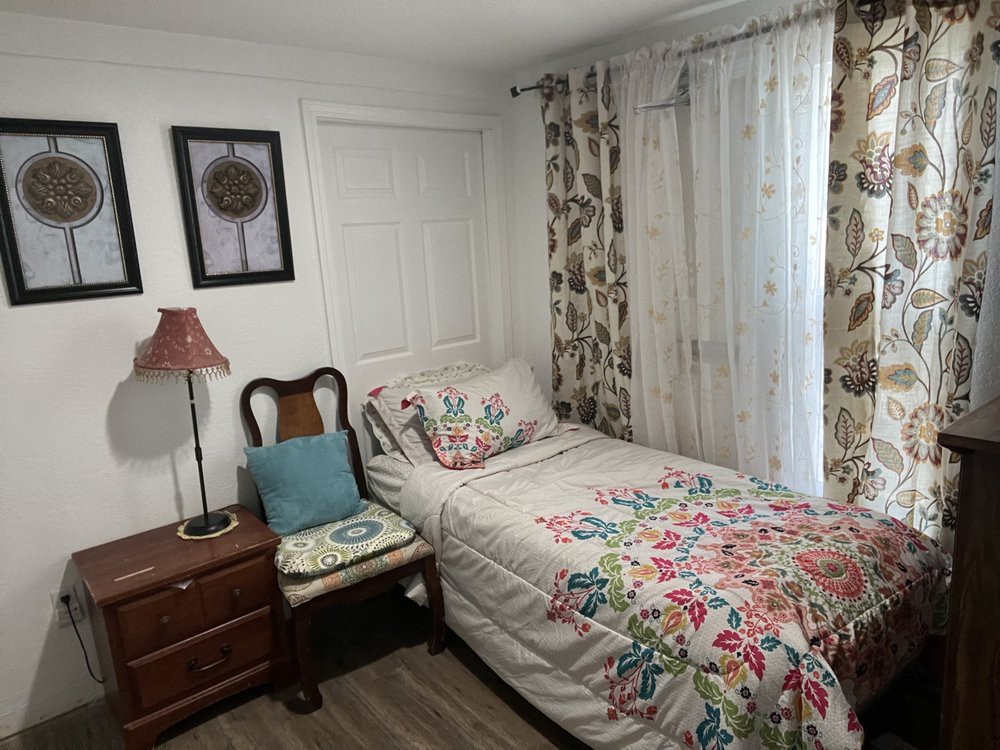 A cozy bedroom with a single bed adorned with floral bedding and matching curtains, complemented by wooden furniture and decorative wall art.