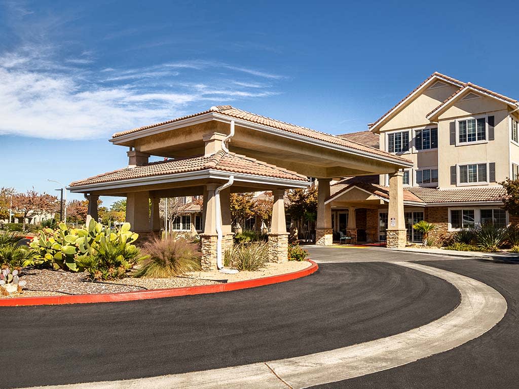 A well-maintained building entrance with a landscaped driveway under a clear blue sky.