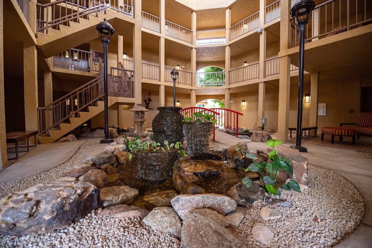 An indoor atrium with a central water feature surrounded by rocks and greenery, enclosed within a multi-story building.