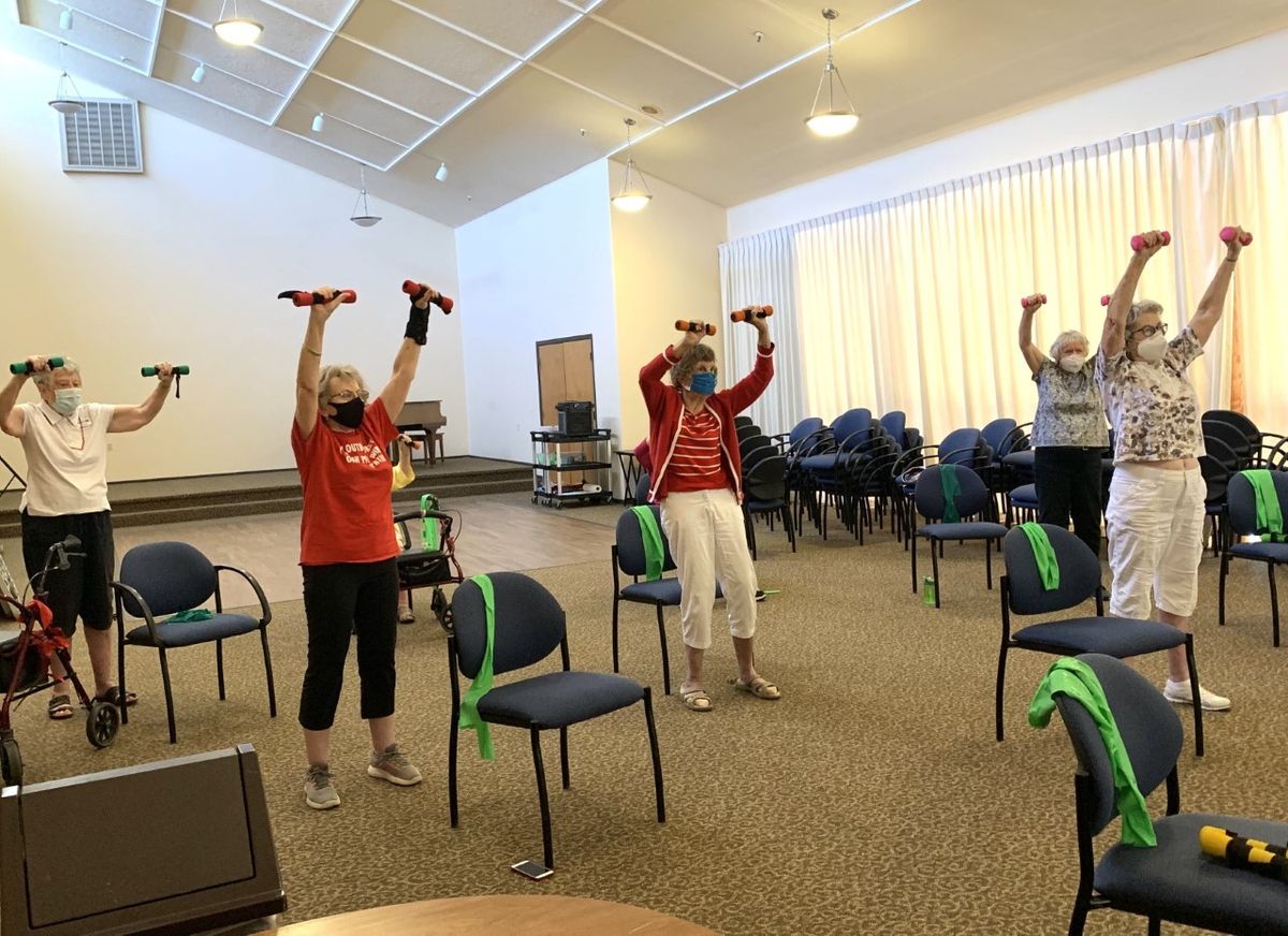 A group of seniors exercising indoors with hand weights.
