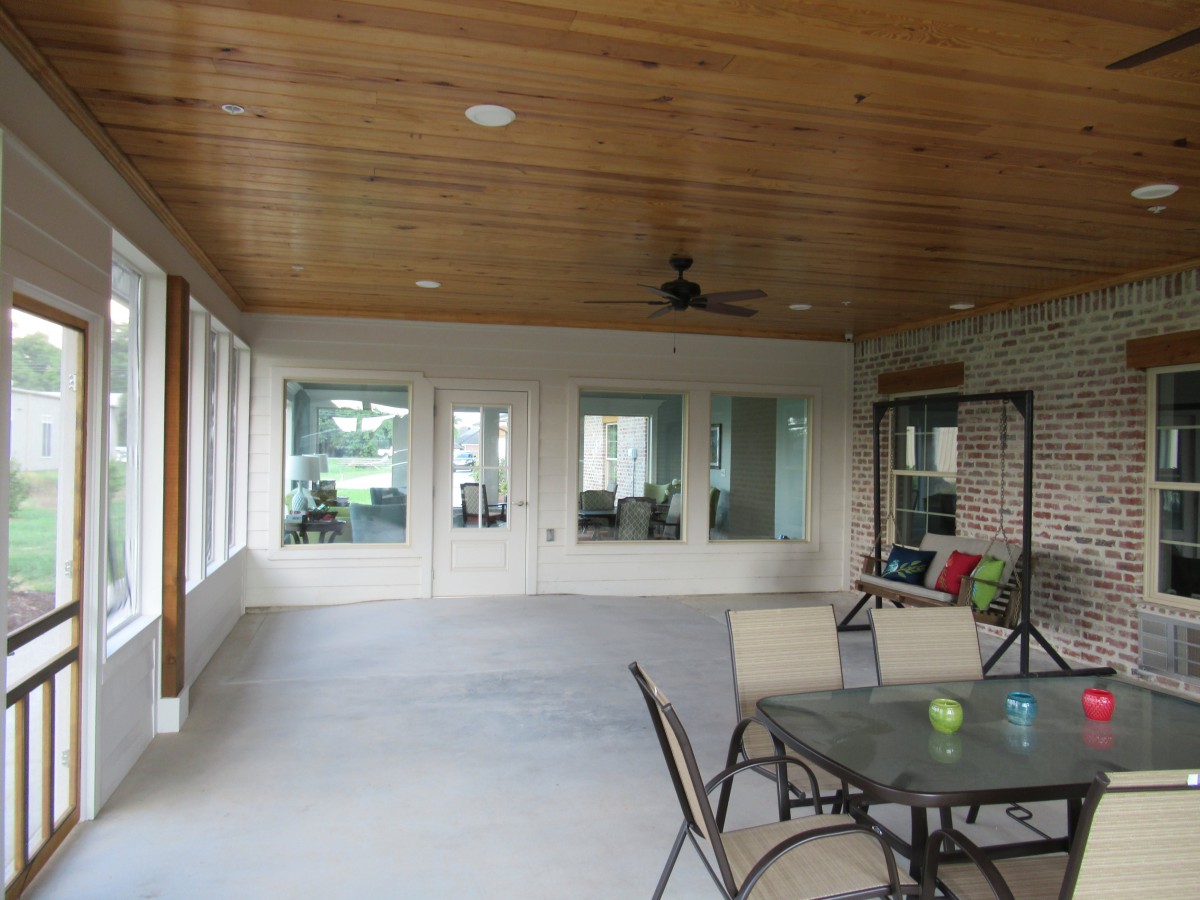 A spacious indoor patio with a table and chairs, featuring large windows and a wooden ceiling with a fan.