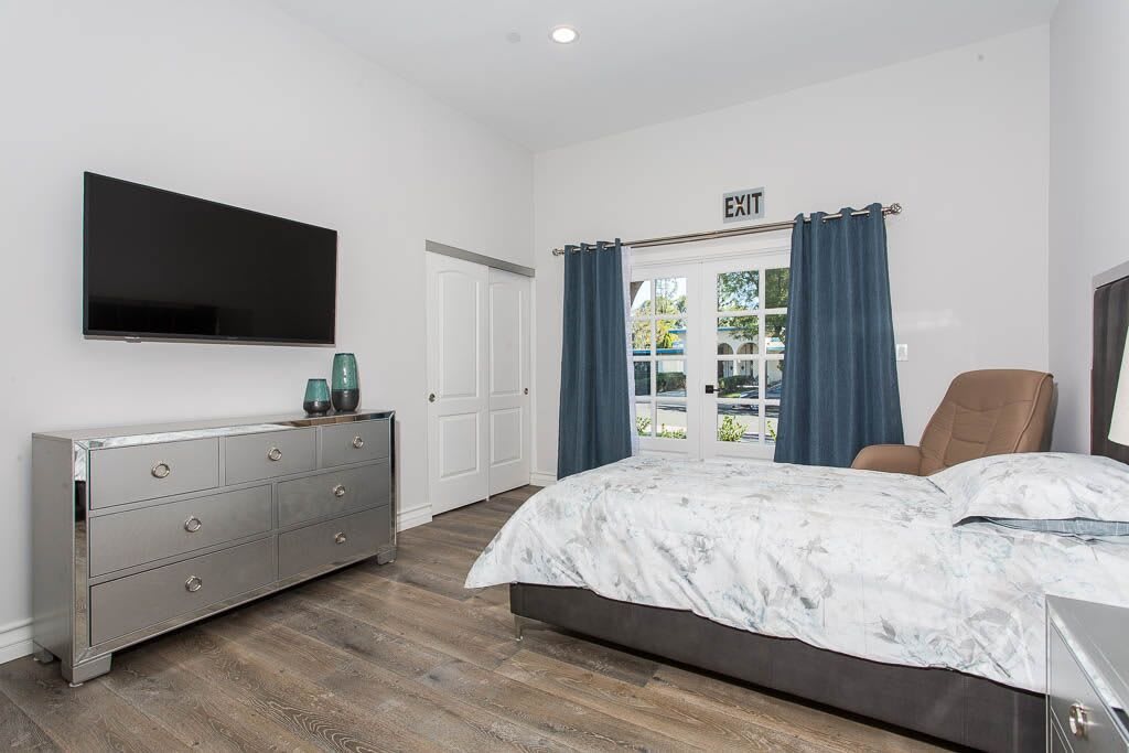 A modern and minimalist bedroom with a large television, blue curtains, and wooden flooring.