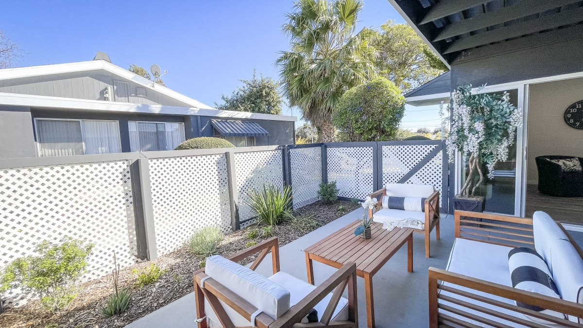 A cozy outdoor patio area with wooden furniture and a lattice fence, surrounded by lush greenery.