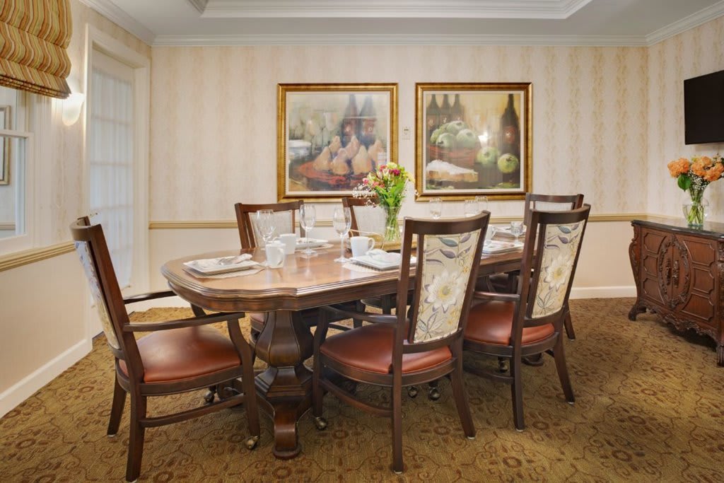 A traditional dining room with a wooden table, upholstered chairs, and framed artwork on the wall.