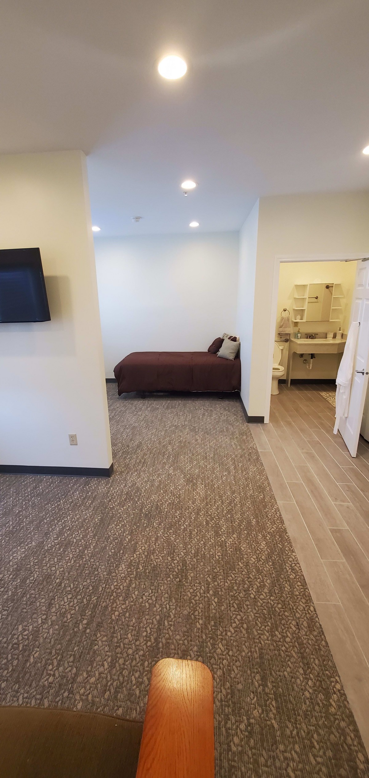A modern hotel room featuring a neatly made bed, wall-mounted television, and an adjoining bathroom.