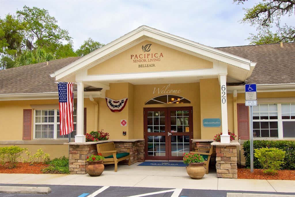 The entrance of a Pacifica Senior Living facility, adorned with American flags and patriotic decorations.