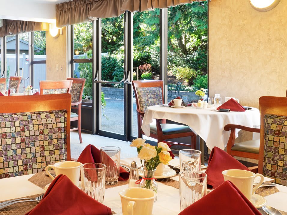 A cozy restaurant dining area with elegantly set tables and a view of the garden through glass doors.