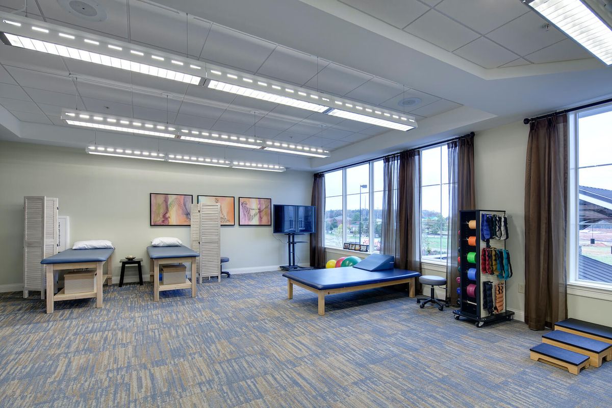 A well-lit physical therapy room with exercise tables and rehabilitation equipment.