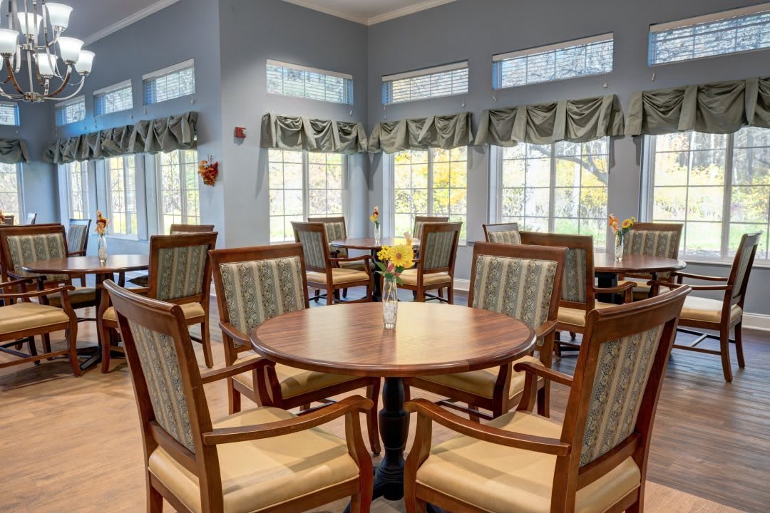 A well-lit dining area with round tables and cushioned chairs near large windows.