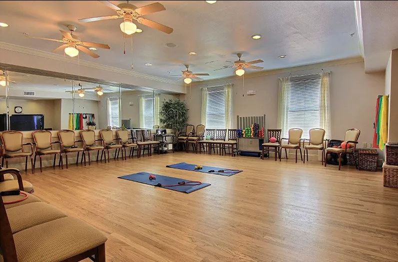 A spacious yoga studio with wooden floors, exercise mats, and chairs arranged along the walls.